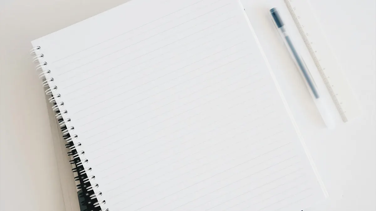 白い机の上に置かれた、何も書かれていない罫線ノートとペン。月の予定と予算を書き出すイメージ。