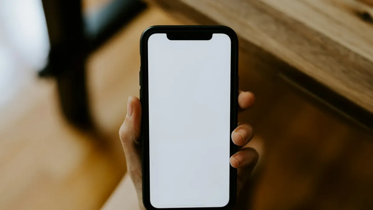 明るい木目のテーブルで、白紙の画面のスマートフォンを持つ手元。契約内容を確認するイメージ。
