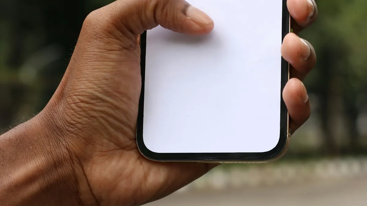 屋外の柔らかな光の中、白紙の画面のスマートフォンを指で操作する手元。確認作業のイメージ。