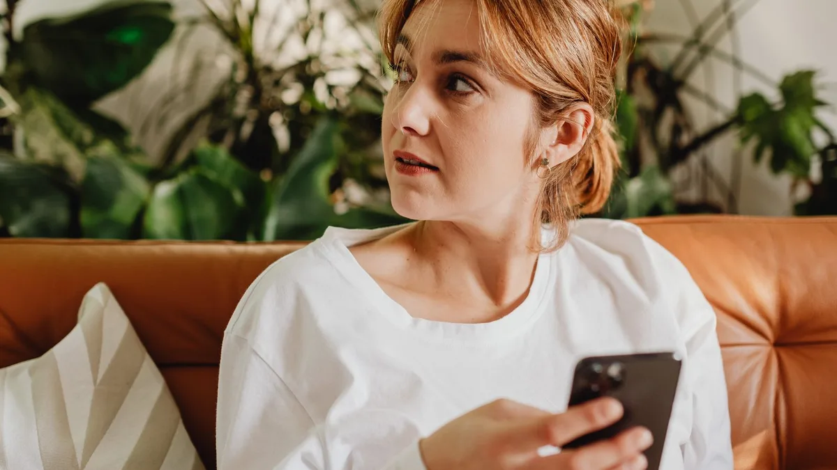 ソファでくつろぎながらスマートフォンを見ている女性。日常のすきま時間にフリマアプリを眺めている雰囲気