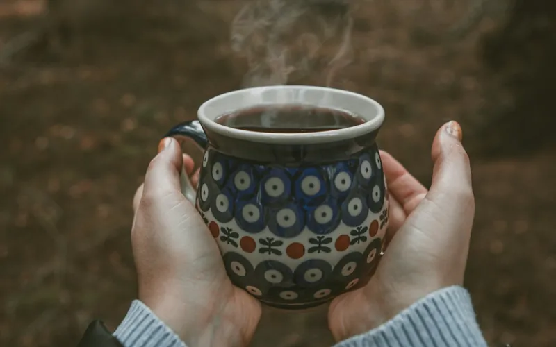 温かい飲み物を両手で包む手元。電気を使わない暖のイメージ。