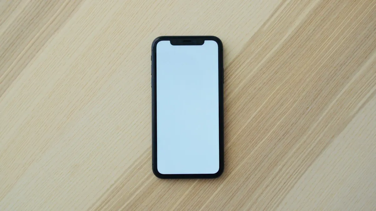 明るい木製テーブルに置かれたスマートフォン。画面はオフで文字は見えない。朝の光が差し込んでいる。