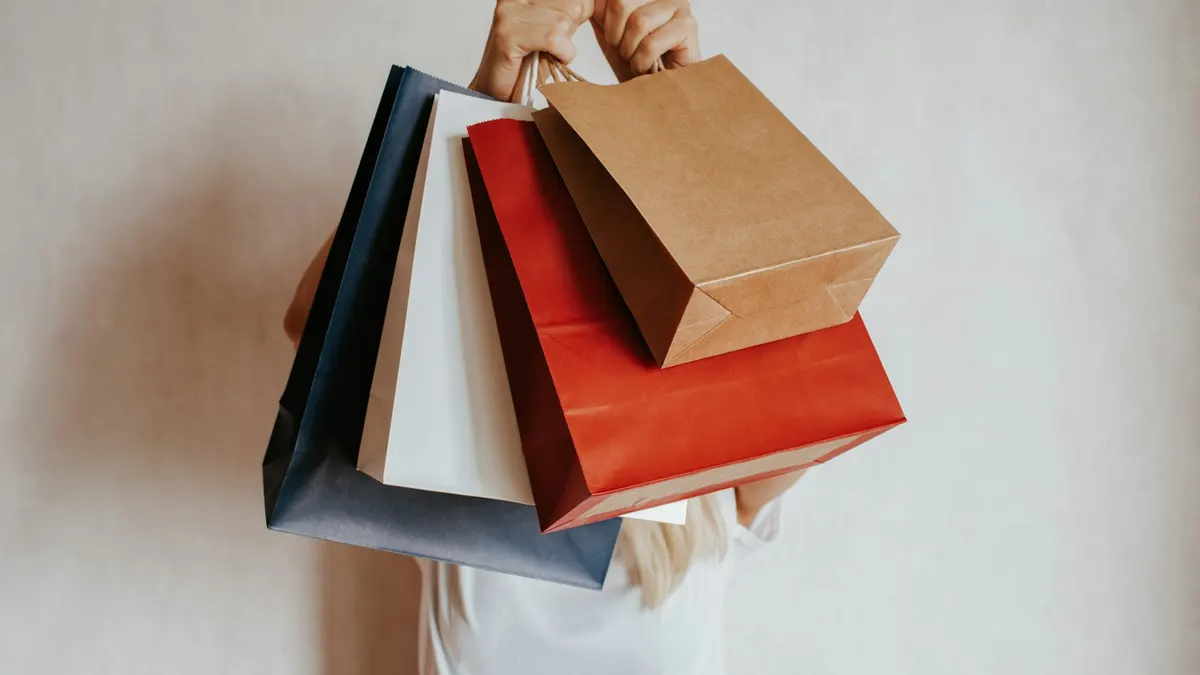 紙製のショッピングバッグを何個も抱えて立つ人物。購入前に見直すイメージ。
