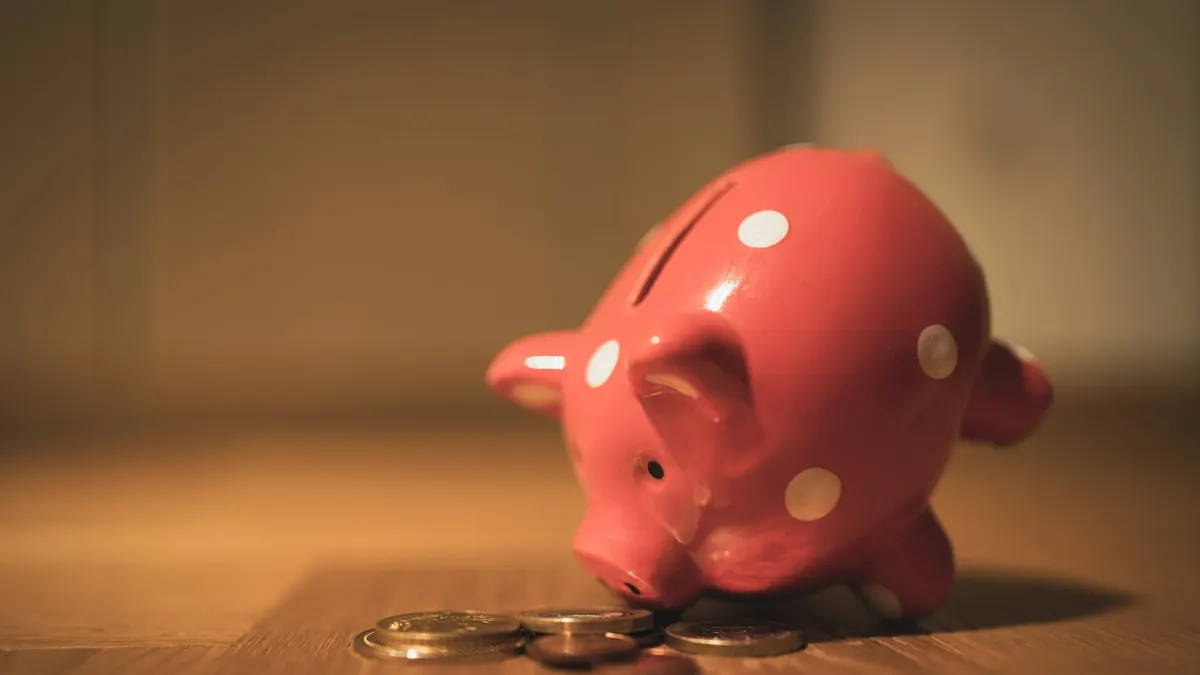 ピンクの水玉模様の貯金箱と硬貨が置かれた暖色の木のテーブル。長期的な家計のイメージ。