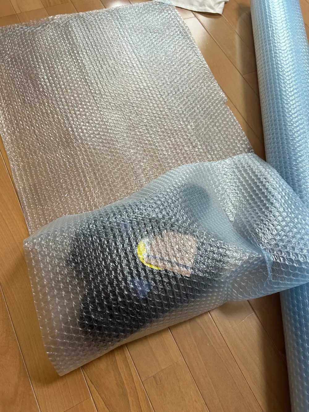 水色の業務用気泡緩衝材のロールから切り出したシートの上に、安全靴を置いて包んでいる途中の写真。