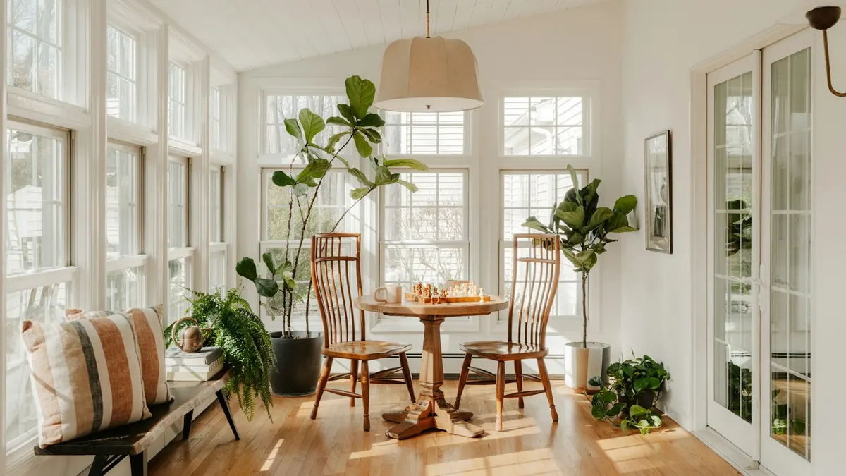 大きな窓から光が差し込む、観葉植物とダイニングテーブルのある明るい部屋。