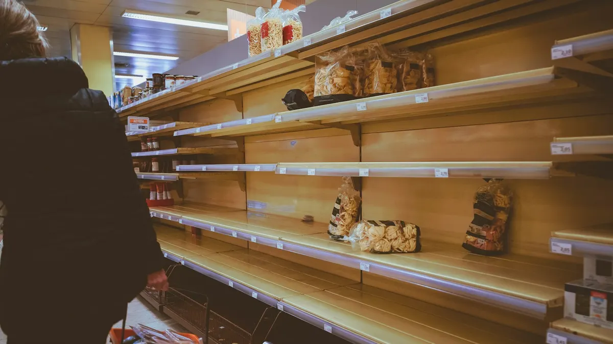店内の棚の前で、商品を手に考えている人のイメージ。