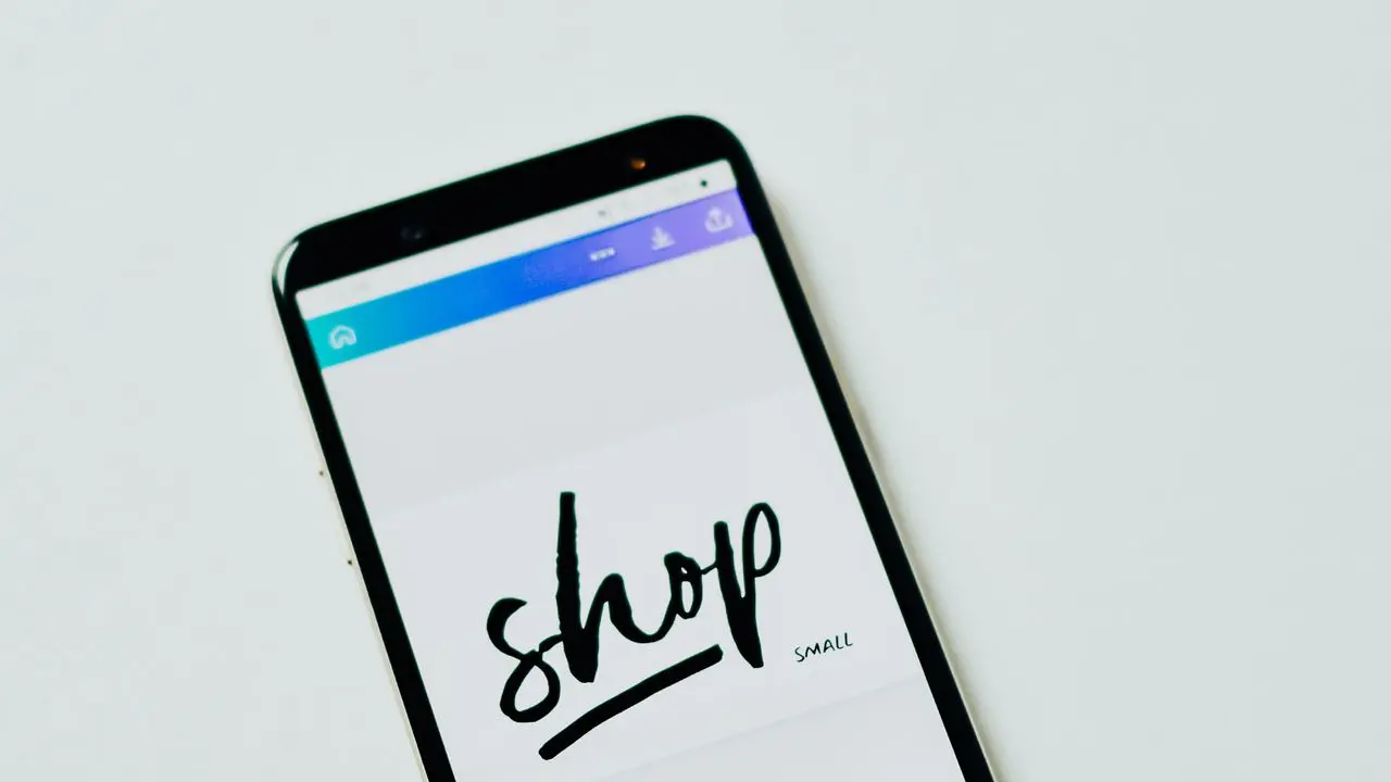 白い背景の前に置かれたスマートフォン。画面に「shop」と書かれたショッピングアプリが表示されている。