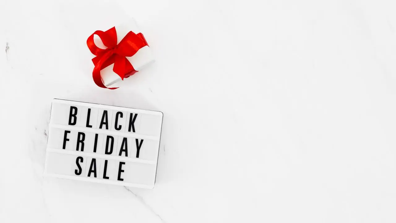 白い大理石の背景の上に「BLACK FRIDAY SALE」と書かれたサインボードと赤いリボンのギフトボックス。セールのイメージ。