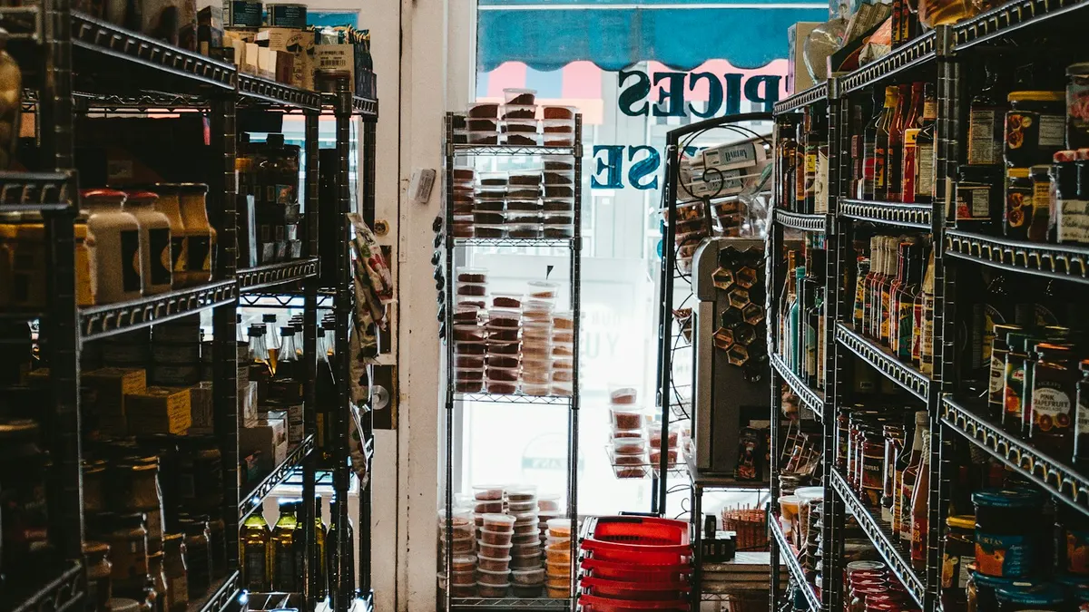 商品がびっしり並んだ店の棚の通路。品ぞろえ・在庫をあらわすイメージ。