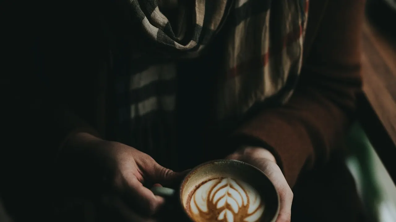 プレイドのマフラーとコーヒーを持つ人物の手元。冬の温かいスタイリングのイメージ。