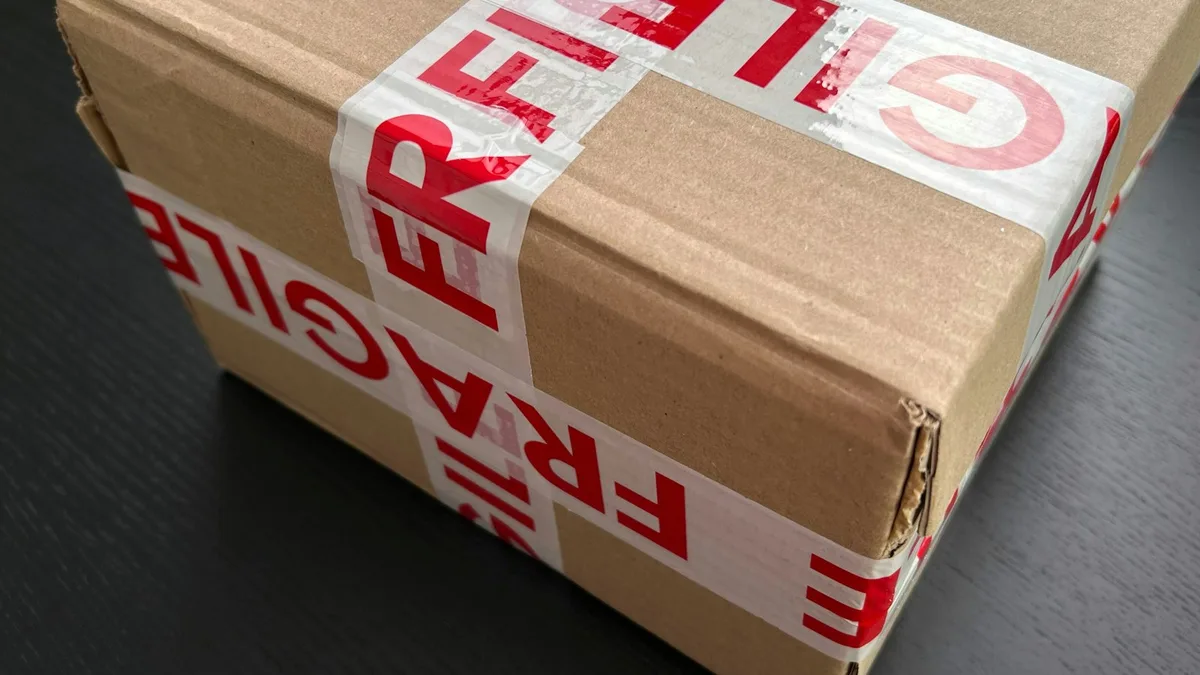 赤い「FRAGILE」の文字が入った梱包テープで十字に封をされた段ボール箱のクローズアップ写真。