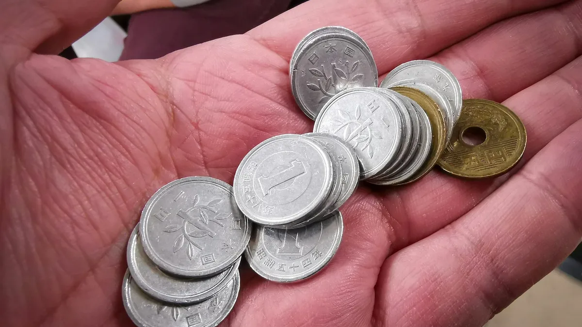 手のひらに乗った日本円硬貨のクローズアップ写真。1円玉が数枚と、五円玉が1枚見える。