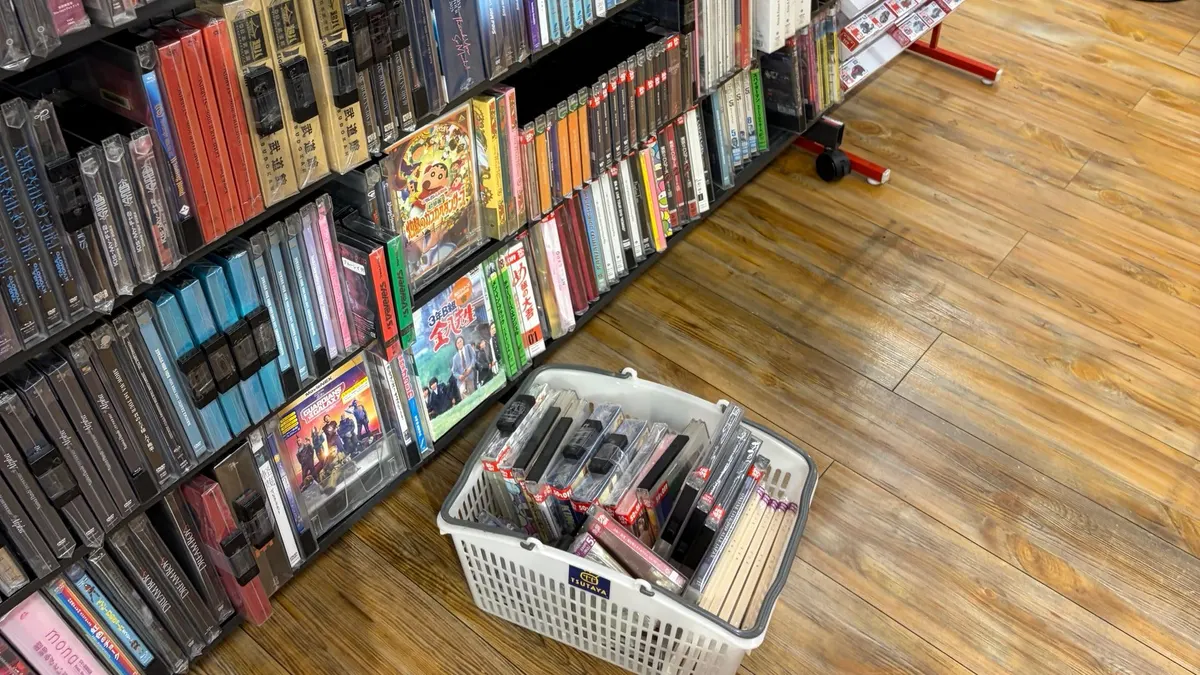 TSUTAYAの店内。CDやDVDがぎっしり並ぶ棚の前に、商品を入れたカゴが置かれている。