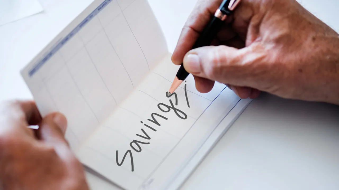 通帳に「Savings」と書き込む手元。家族のための貯蓄口座のイメージ。