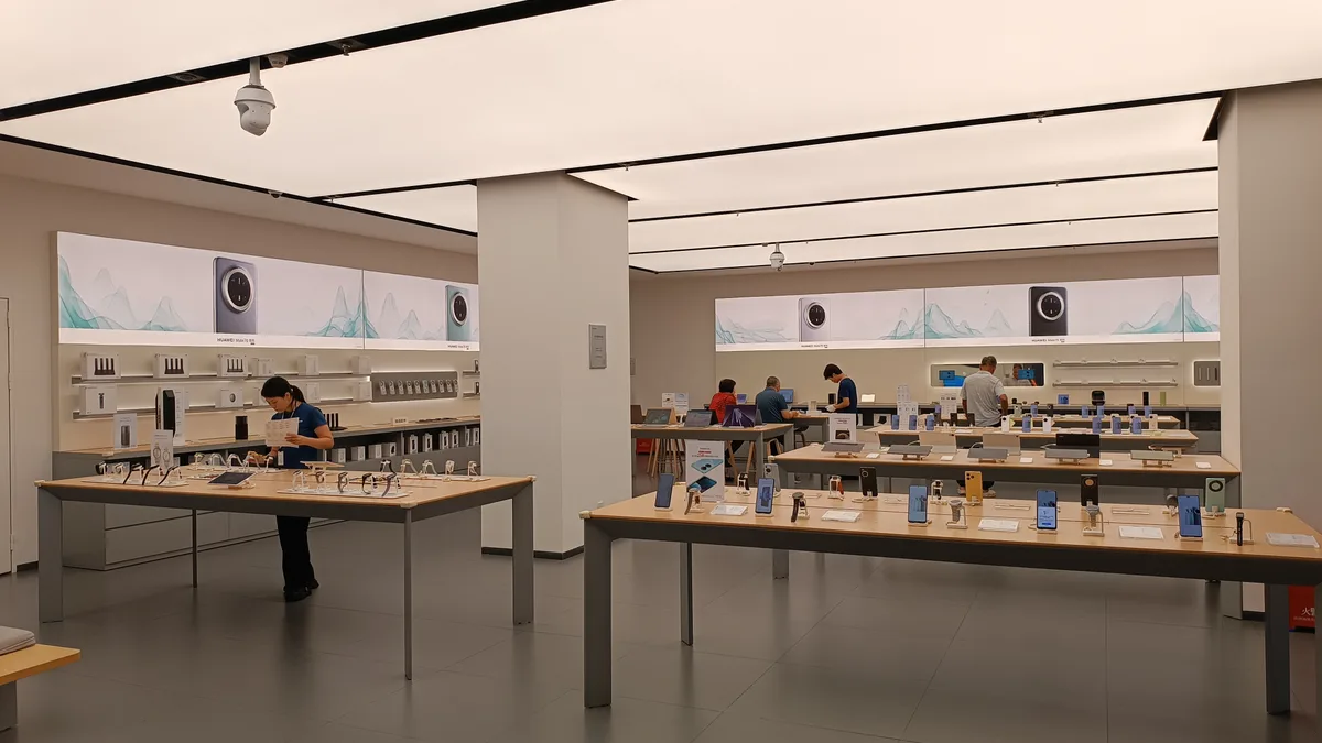 家電とスマートフォンの売り場。商品が並ぶテーブルの前で、店員と客が実機を確認している。