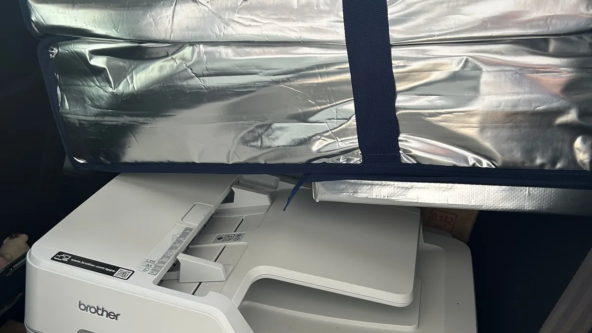車の後部座席に積んだ中古の複合機。ブラザー製のプリンタが横倒しで載っている