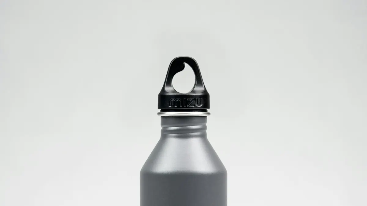 木製のテーブルの上に、黒いキャップの付いたステンレス製の水筒が1本、白い背景の前に立っている接写。