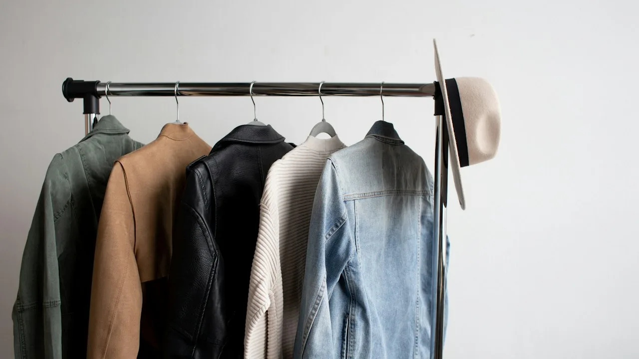 洋服掛けに吊るされたジャケットやコートが並ぶ様子。防寒具を賢く揃えるテーマのヒーロー画像。