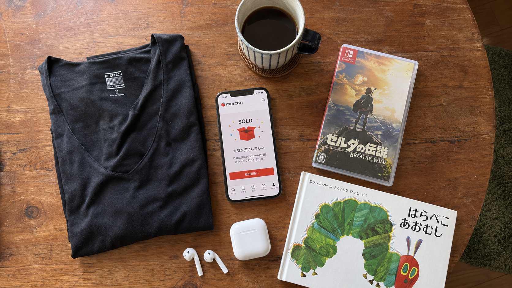 出品予定品の俯瞰（ヒートテック・ゲームソフト・AirPods・絵本とSOLD通知のスマホ）