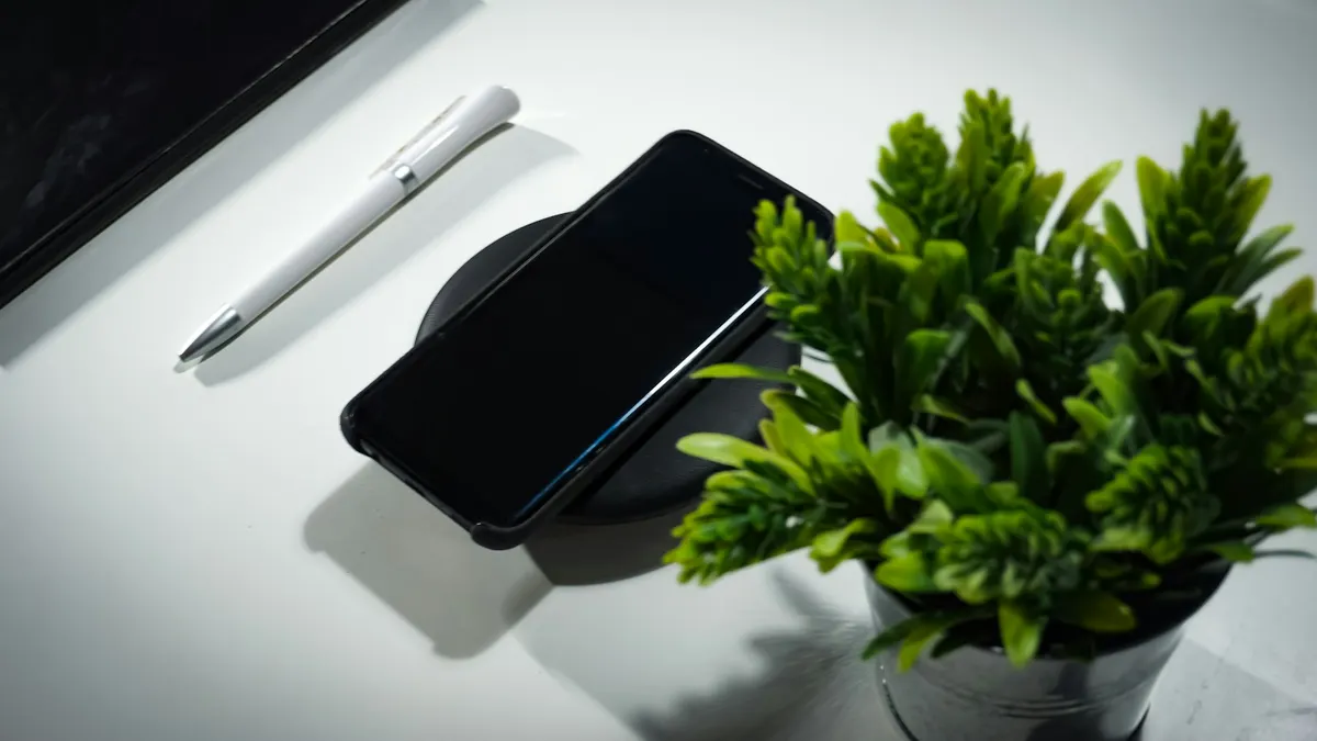 机の上でワイヤレス充電されているスマートフォンと小さな観葉植物