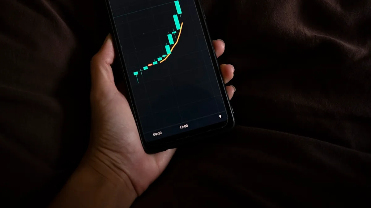 スマートフォンの画面に価格の推移グラフが表示されているシーン。売り切れ相場チェック・データ確認のイメージ。