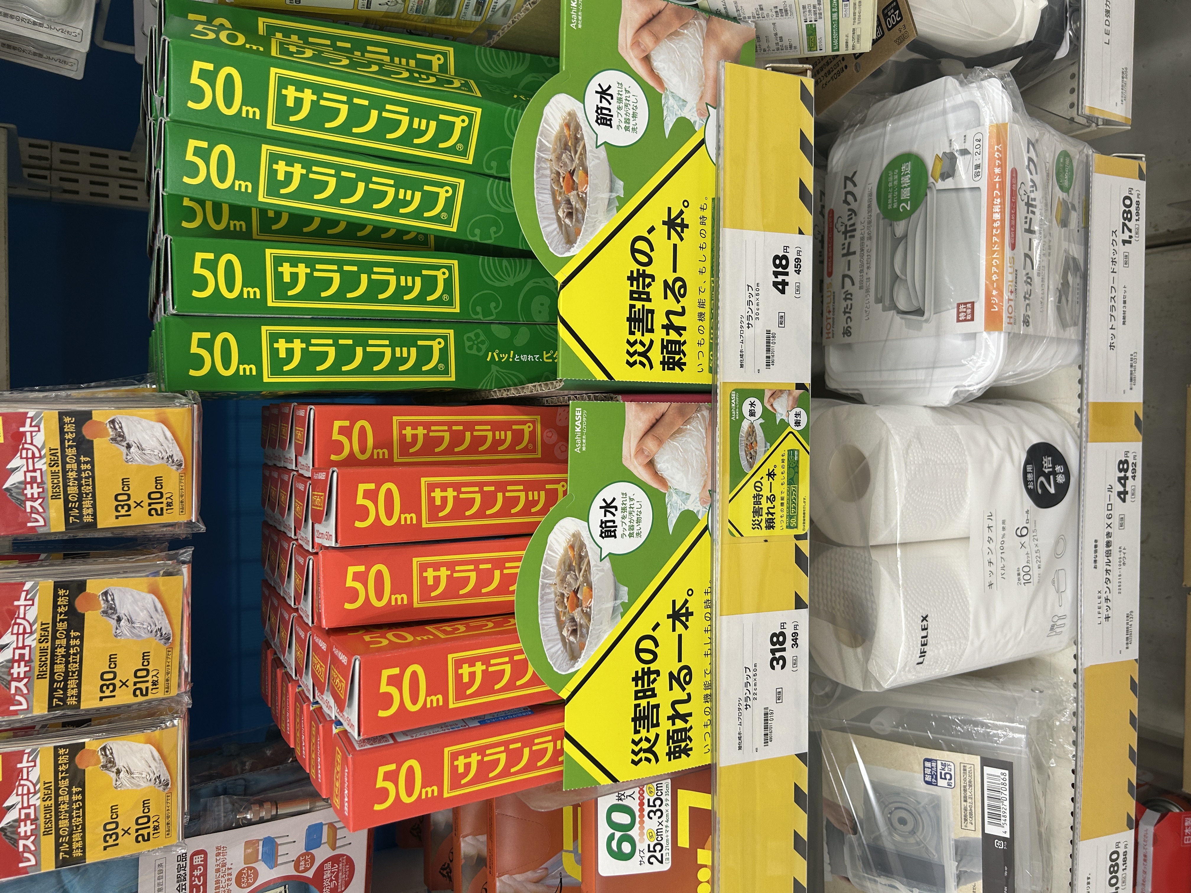 ホームセンターのサランラップ棚（緑・赤の50m箱が並ぶ陳列）