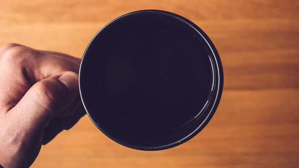 木のテーブルの上で、コーヒーの入ったカップを持っている手元