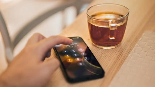 カフェの木製テーブルでスマートフォンを操作する手元。ネットで買い物を比較するイメージ。