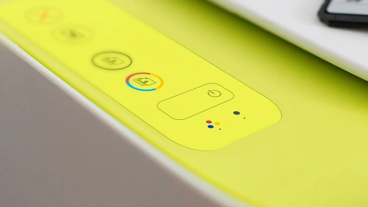 白い家庭用プリンターの操作パネルを斜め上から撮った接写。蛍光イエローグリーンのパネル面に、電源ボタンと、カラーコピー・モノクロコピーを示すアイコンボタンが縦に並び、小さなインジケーターランプが点いている。奥には白い本体の天面が続いている。