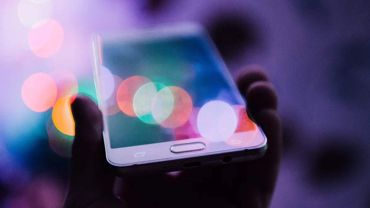 暗い場所で手に持ったスマートフォンの画面に、色とりどりの光がぼやけて映り込んでいる様子