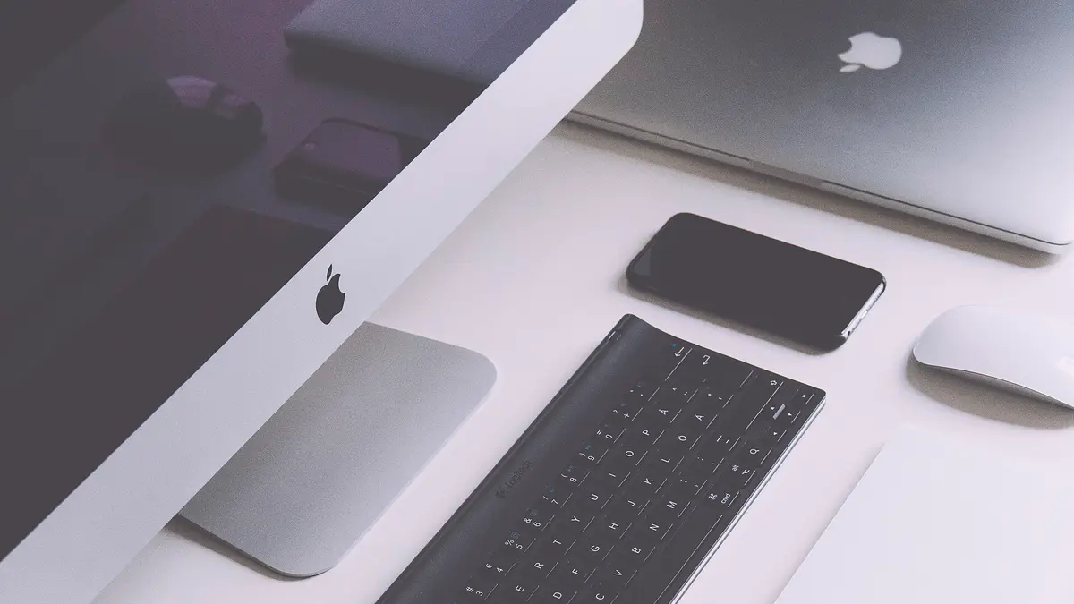 白いデスクの上にiMac・ノートパソコン・スマートフォン・キーボード・マウスが並べて置かれている様子