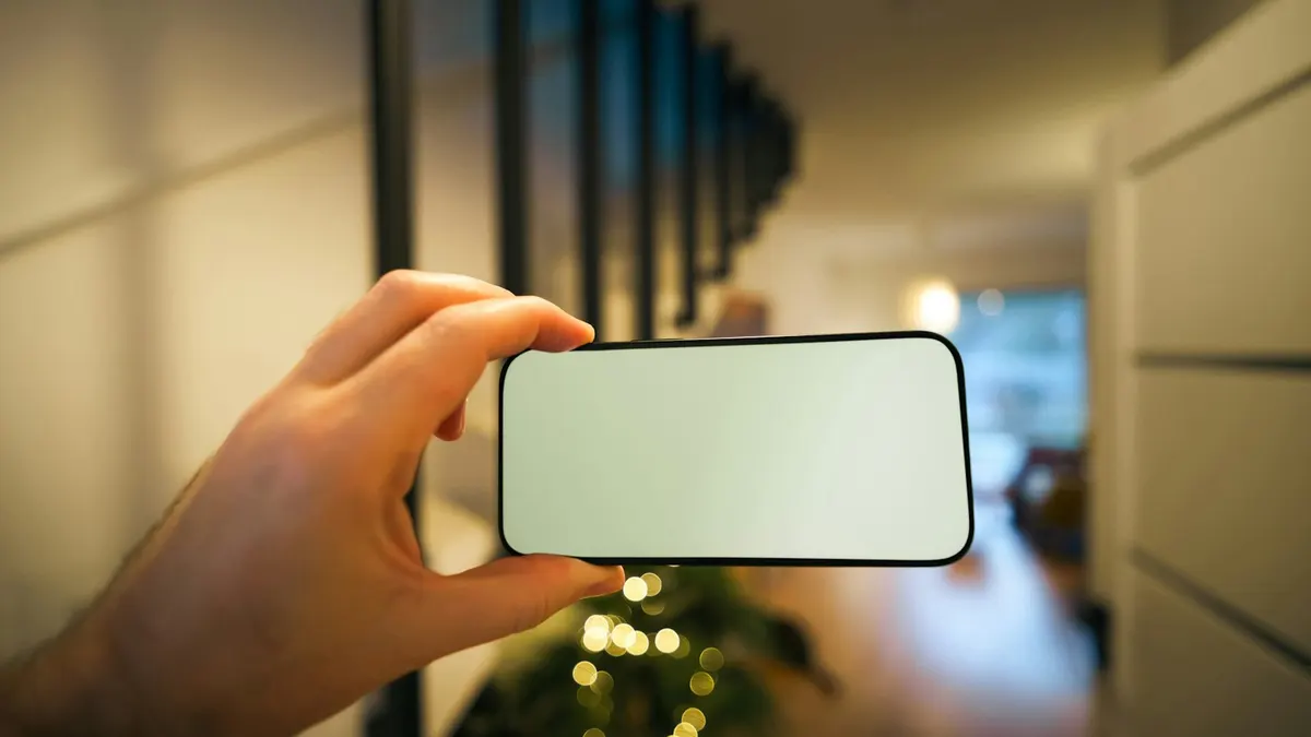 室内で無地の画面のスマートフォンをかざす手元。Amazonのタイムセールを確認するイメージ。