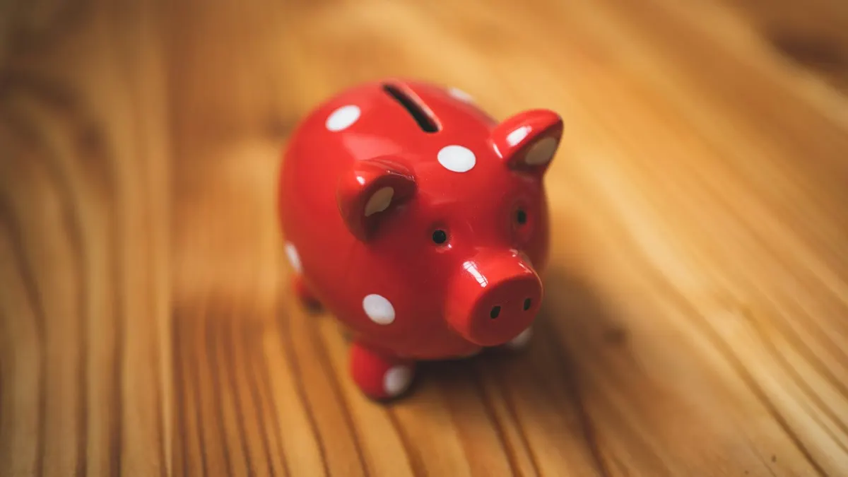 木製のテーブルに置かれた赤い水玉模様の豚の貯金箱。ポイントを貯めて次に回すイメージ。