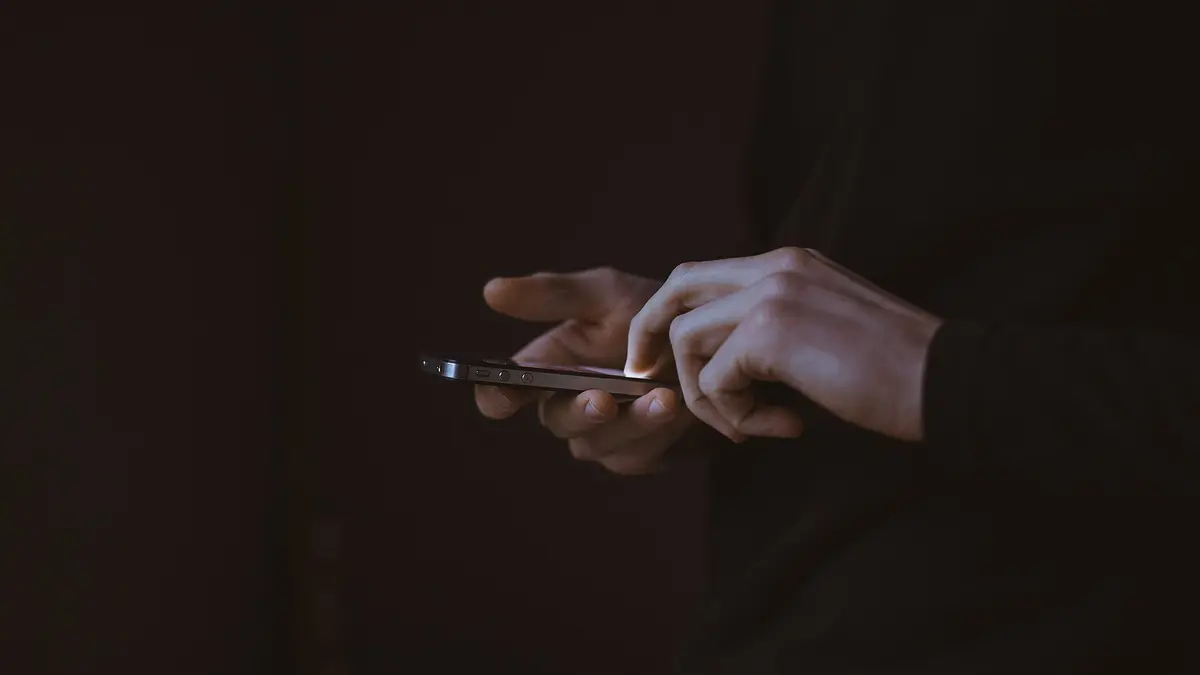 暗い室内でスマートフォンを両手で操作している手元