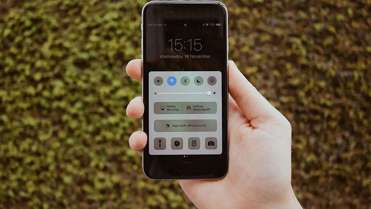 緑の植え込みを背景に、片手でスマートフォンを持ちコントロールセンター画面を表示している手元のクローズアップ