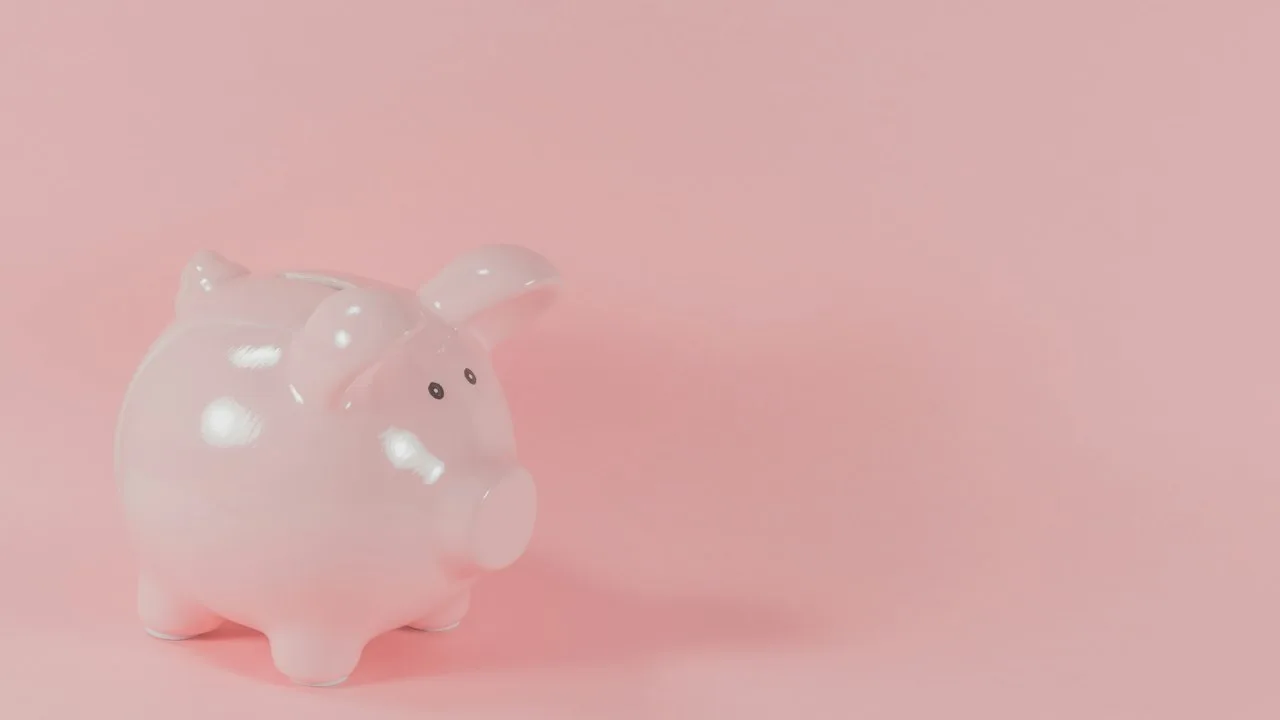 ピンク色の背景に置かれた白い陶器の豚の貯金箱の写真。シンプルでかわいらしいポイント蓄積のイメージ。