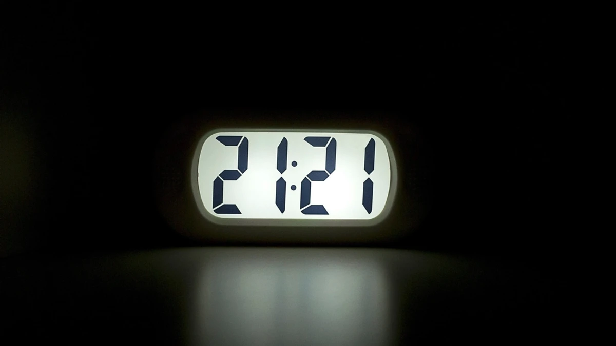 暗い部屋で光るデジタル時計の表示。21時21分を示している。