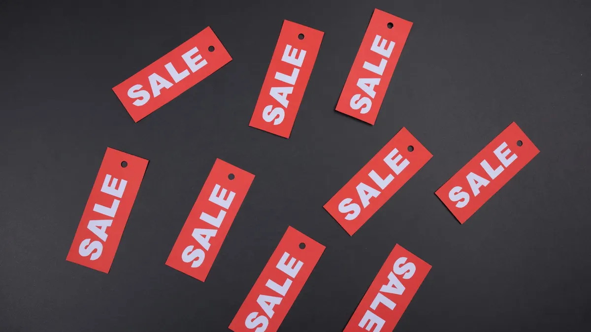 濃いグレーの背景に、白抜きでSALEと印刷された赤い紙タグが散らして並べられている。