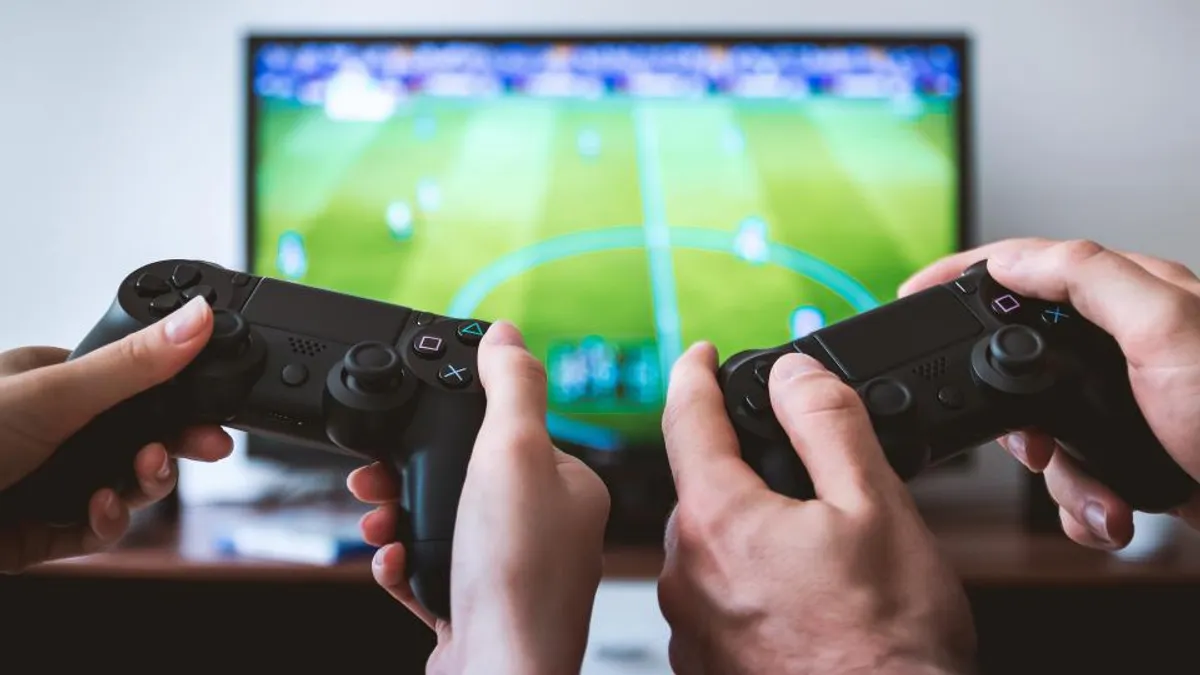 テレビでサッカーゲームを表示しながら、2人がゲームコントローラーを操作している手元