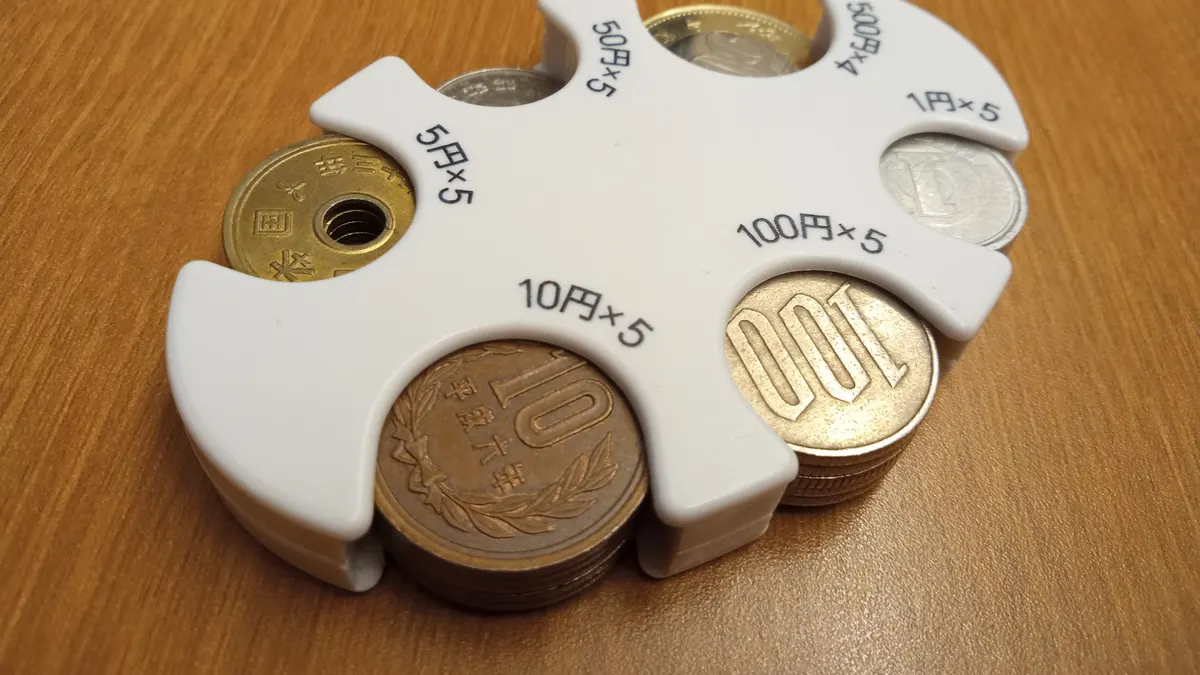 白いコインホルダーに1円・5円・10円・50円・100円・500円の硬貨がそれぞれ収まっている。木目のテーブルの上に置かれ、各枠に「10円×5」「100円×5」などの表示がある