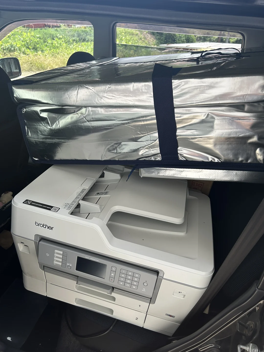 車の後部座席に積み込んだ中古のブラザー複合機。上に銀色の保冷バッグが重ねて置かれている
