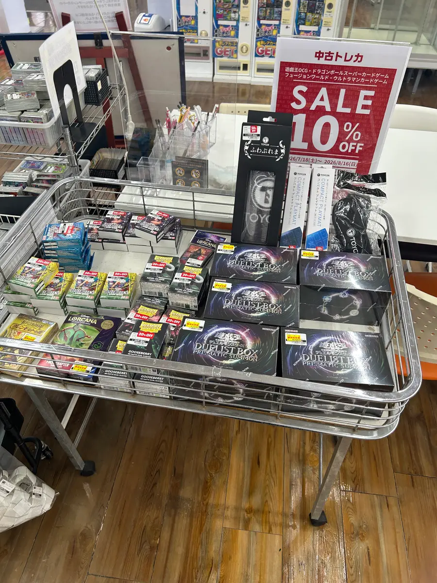 TSUTAYA店内のワゴン。「中古トレカ SALE 10% OFF」の赤いPOPが立ち、ワゴンの上にTOYGERのプレイマット、遊戯王のDUELIST BOX、LORCANA、50%OFFラベルの付いた商品が並んでいる。