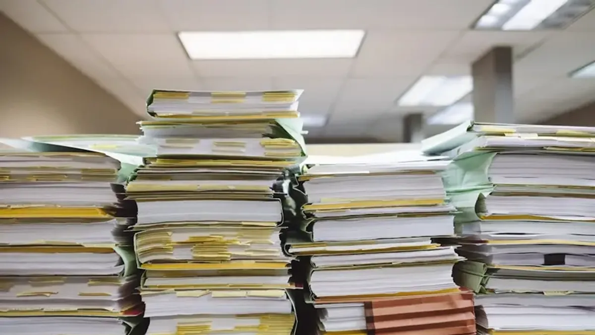 事務室に高く積み上げられた大量の書類の山。付箋やインデックスがはさまっている。