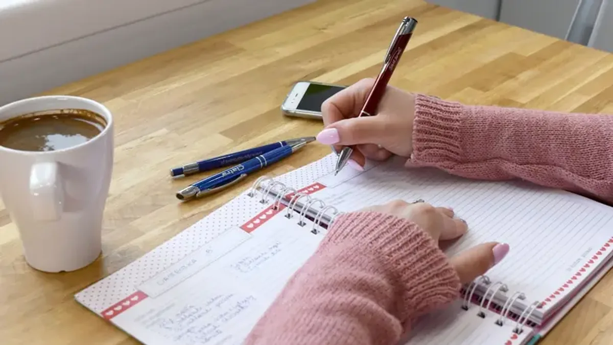 ノートに数字や記録を書き込んでいる手元。日々の記録をつけるシーン。