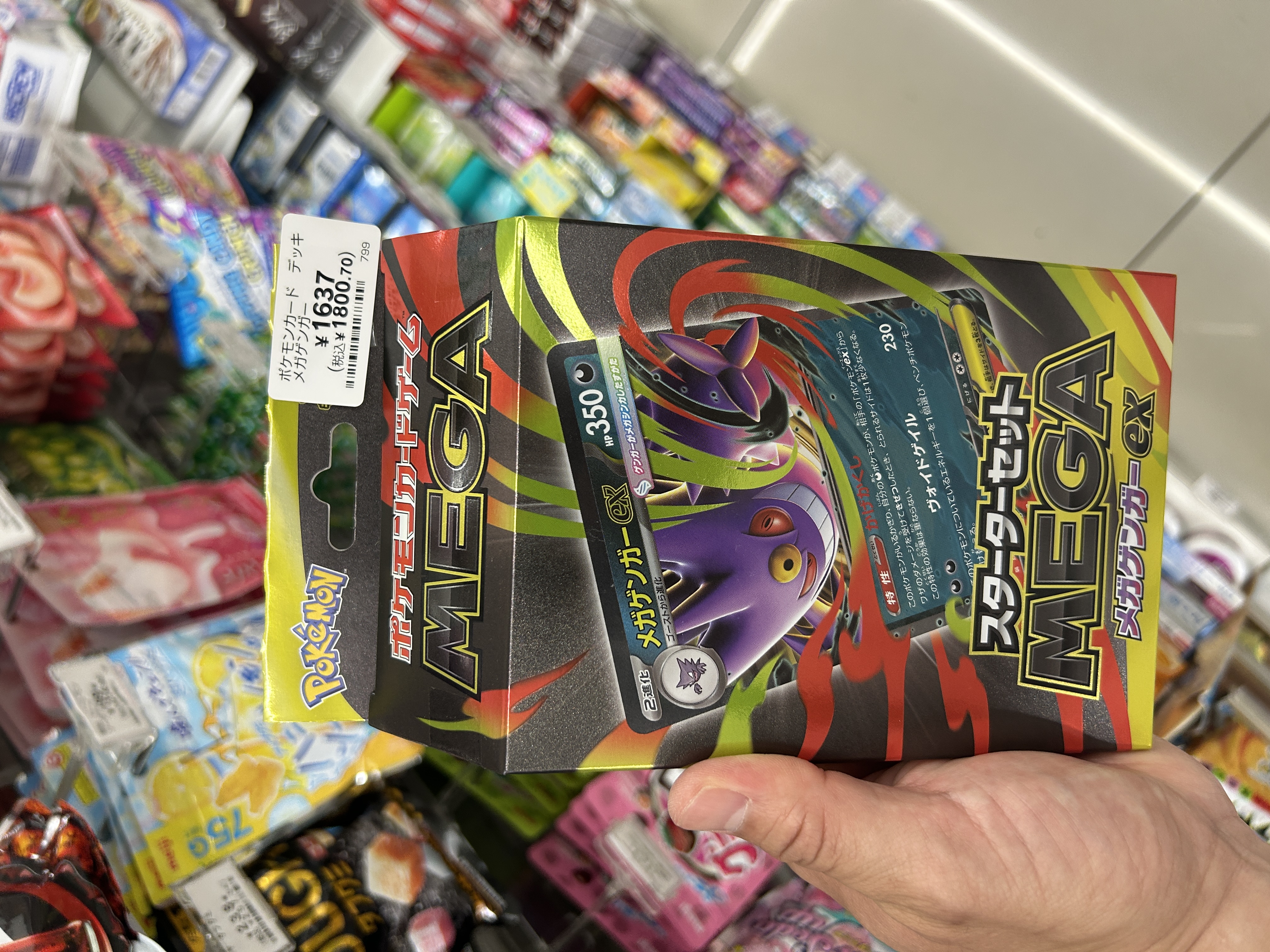 セブンイレブン店内でポケモンカード MEGA スターターセット メガゲンガーex(値札¥1,800)を手に持つ様子
