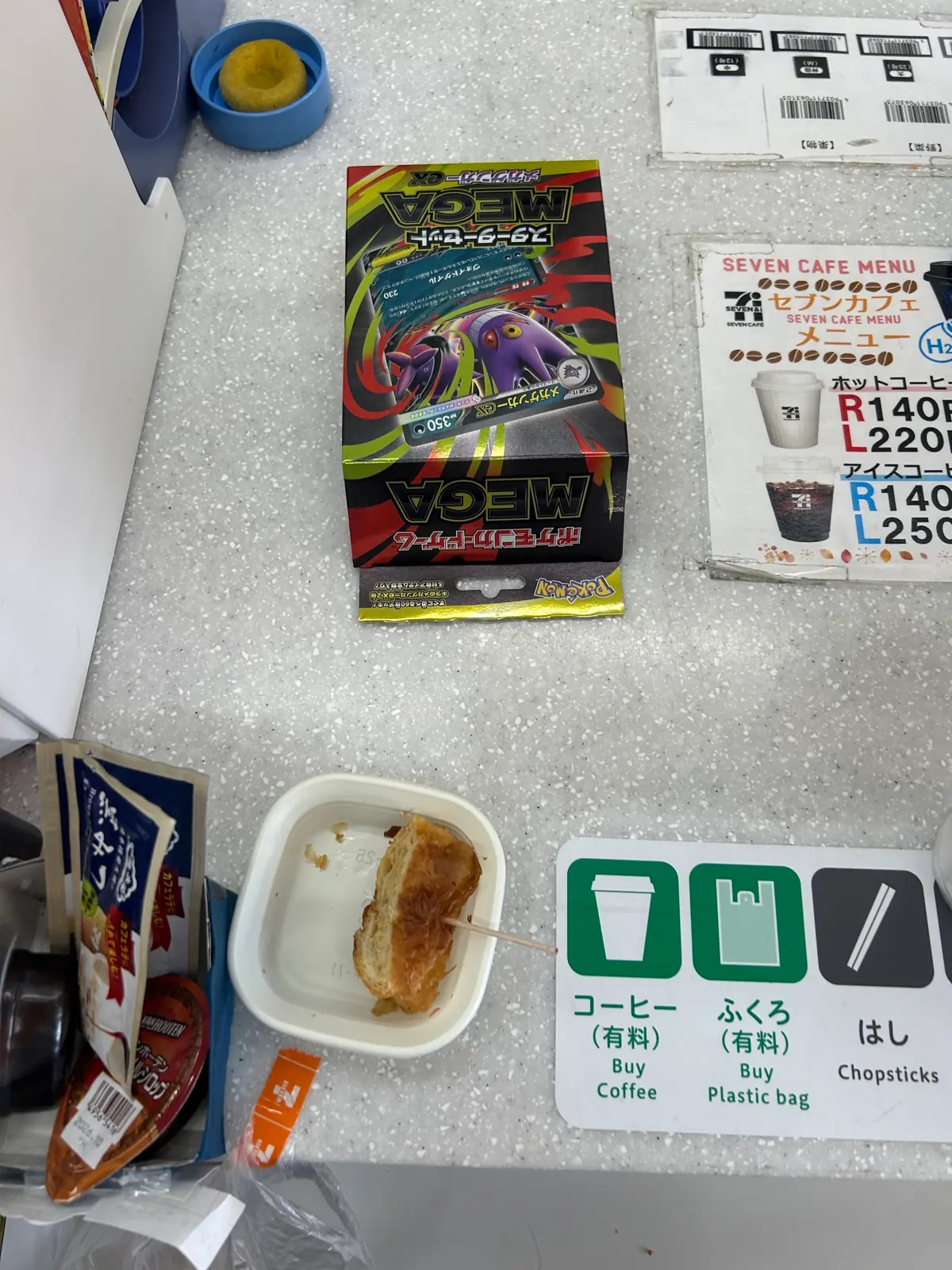 店内のカフェカウンターでコーヒーを飲みながら、戦利品のMEGAスターターセットex 2個を眺めて一服している様子