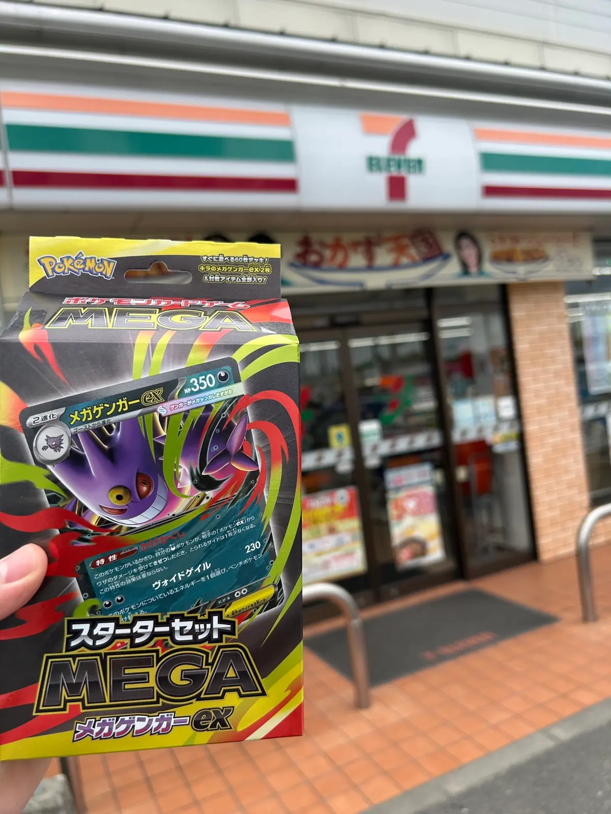 店外でセブン-イレブンの看板を背景に、2店舗で確保したポケカ MEGAスターターセットex 2個を手に持つ様子