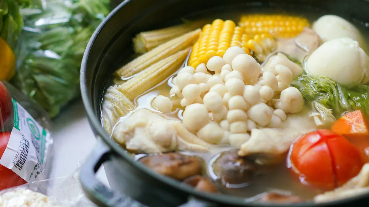 黒い土鍋にコーン・えのき茸・トマト・鶏肉などの具材が入り、出汁で煮えている鍋料理の写真。